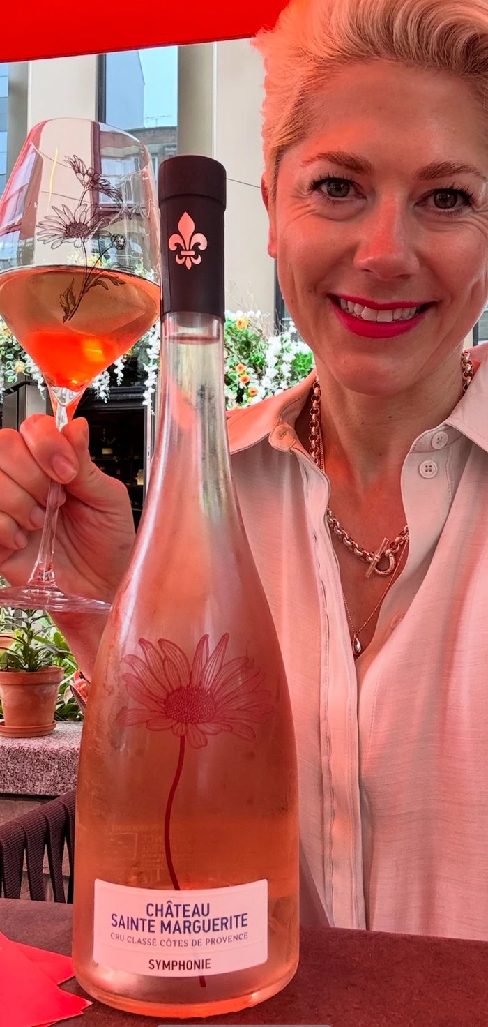 Smiling woman holding a glass of rosé beside a Château Sainte Marguerite bottle