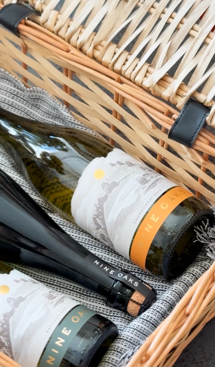 Nine Oaks wine bottles nestled in a woven basket with grey fabric