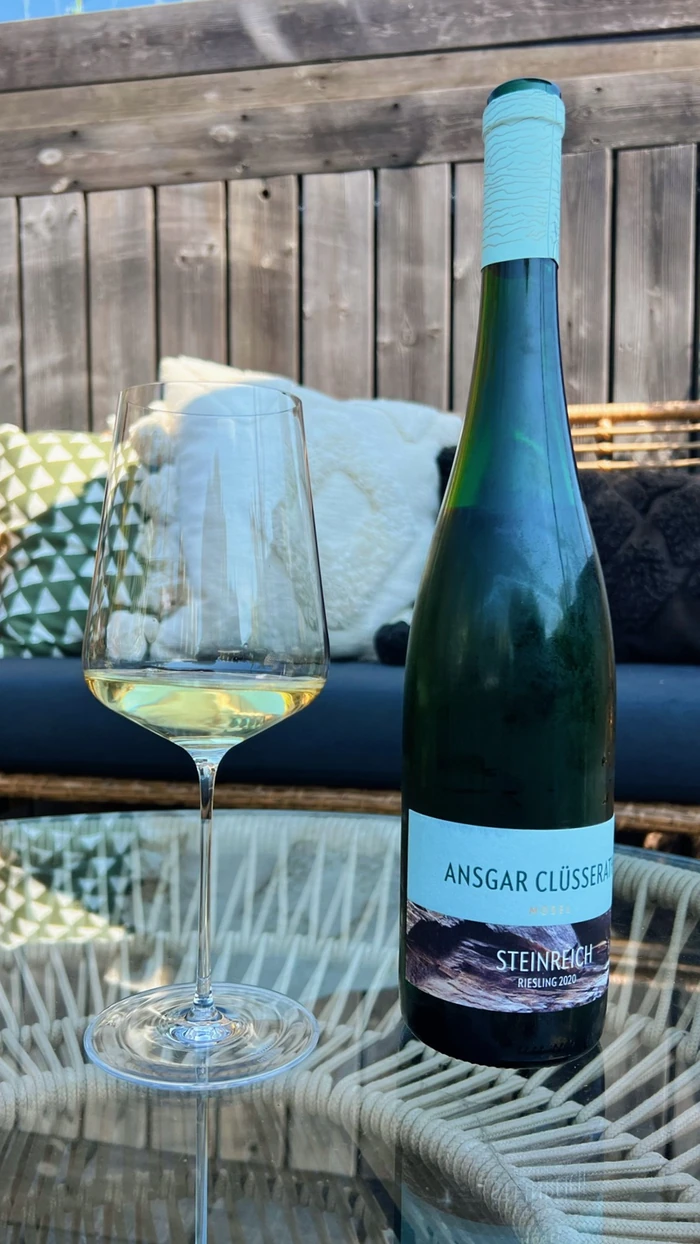 Ansgar Clüsserath Steinreich Riesling bottle beside a glass of white wine on an outdoor table