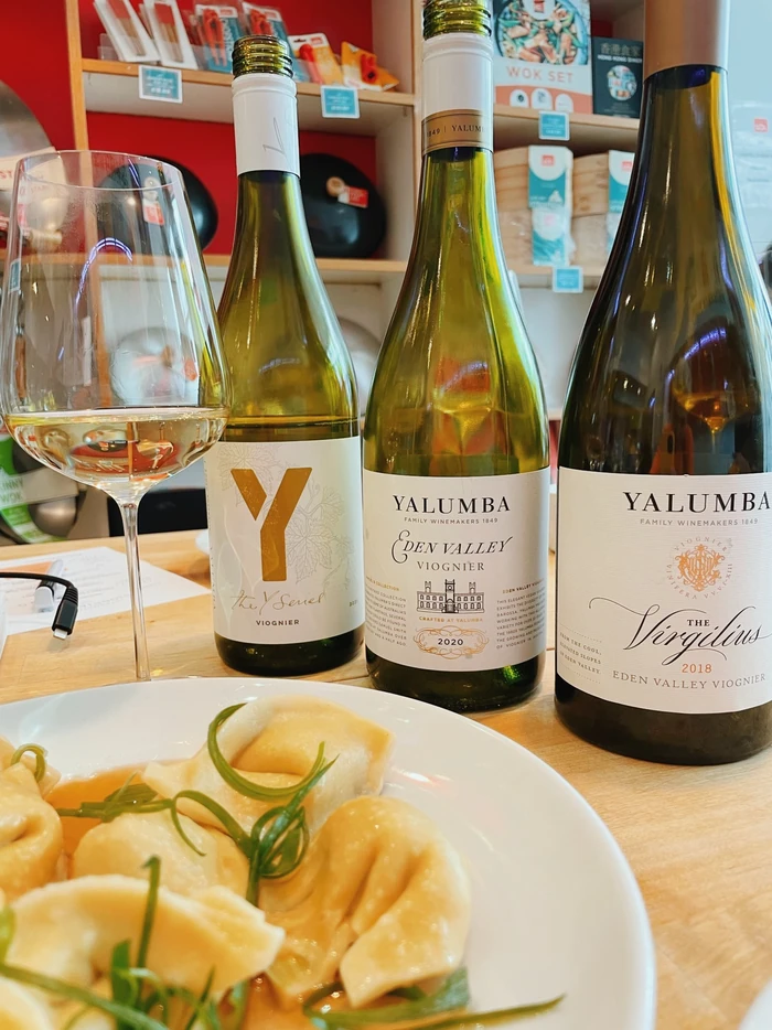 Three Yalumba Viognier bottles and a glass of wine beside a plate of dumplings