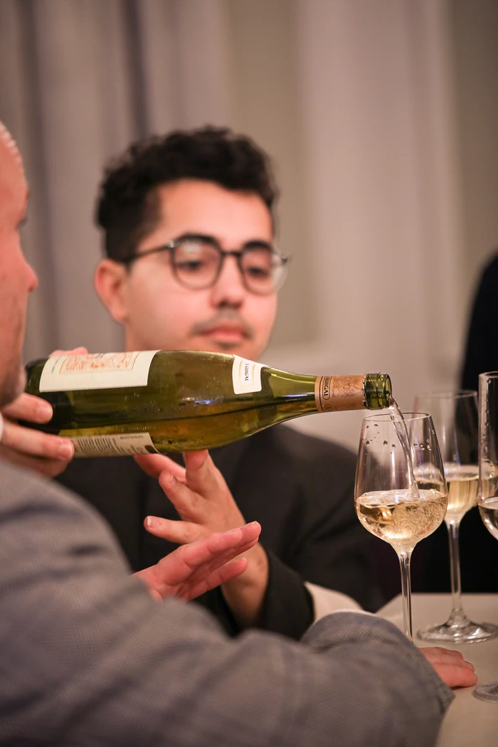 Wine being poured into a tasting glass as guests watch at a table