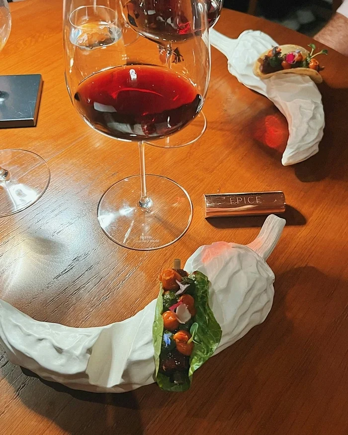 Red wine in a labelled glass beside artistic small plates at EPICE