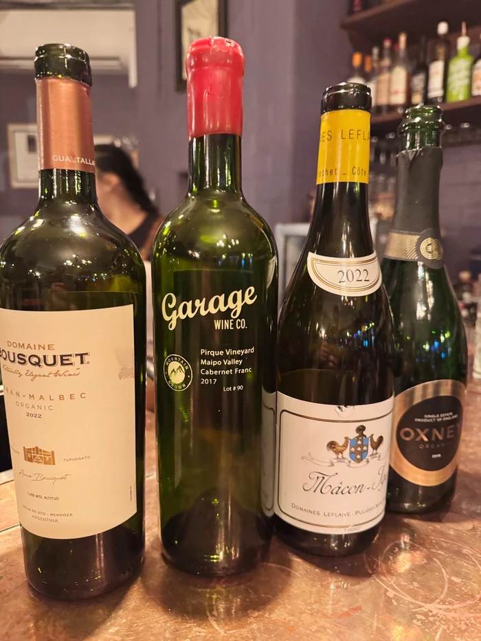 Four wine bottles displayed on a wooden bar, including Garage Wine Co. Cabernet Franc and Domaine Bousquet Malbec