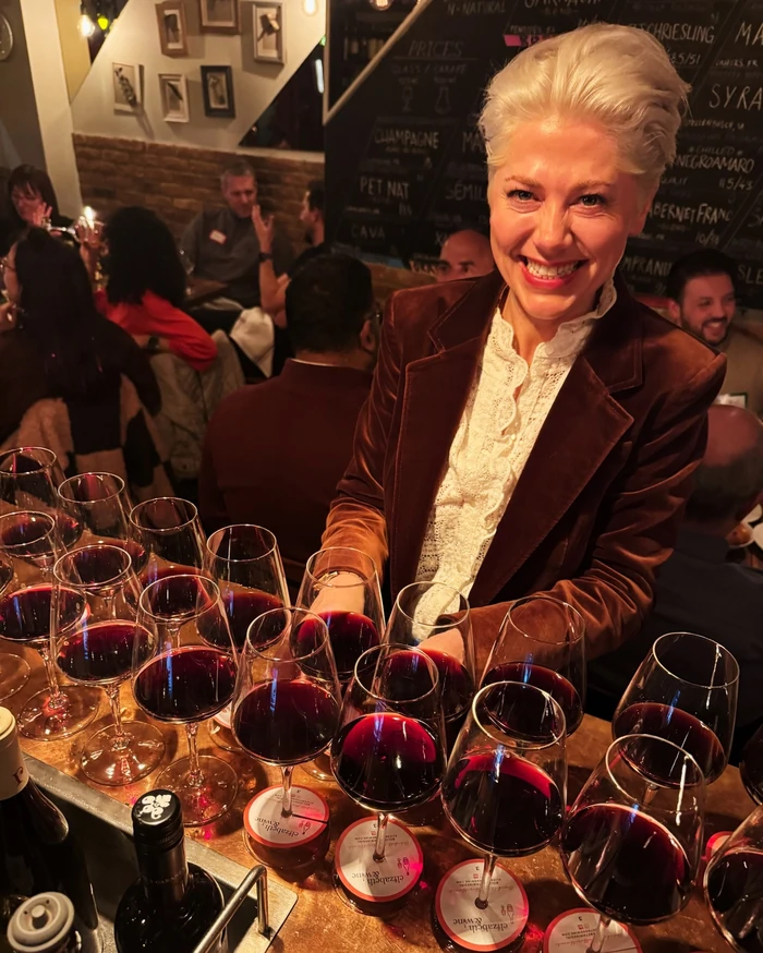 Smiling woman beside a table covered with glasses of red wine at a tasting event