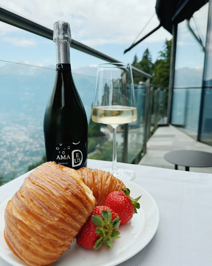 Prosecco, a filled wine glass, croissant and strawberries on a table beside a glass-walled terrace