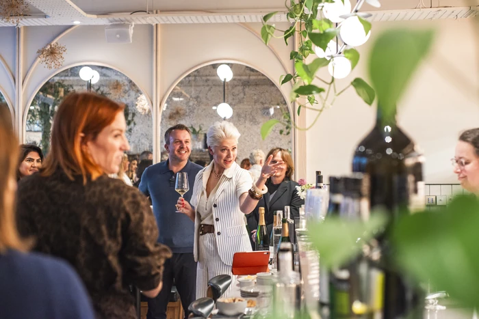 Wine tasting guests gathered around a bar as a presenter holds a glass and speaks