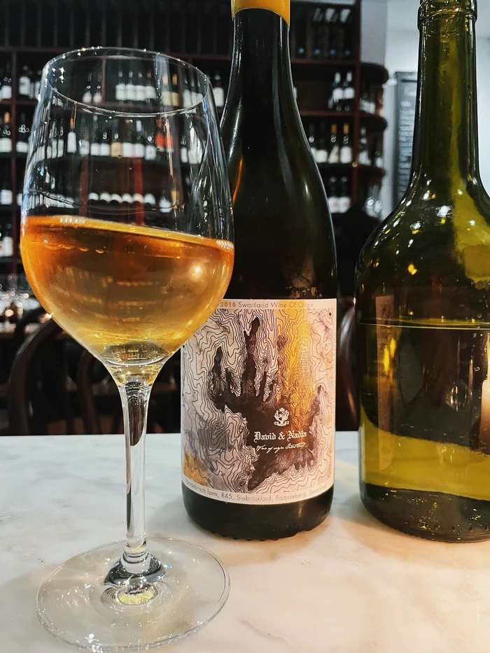 Glass of amber wine beside a David & Nadia 2018 Swartland wine bottle