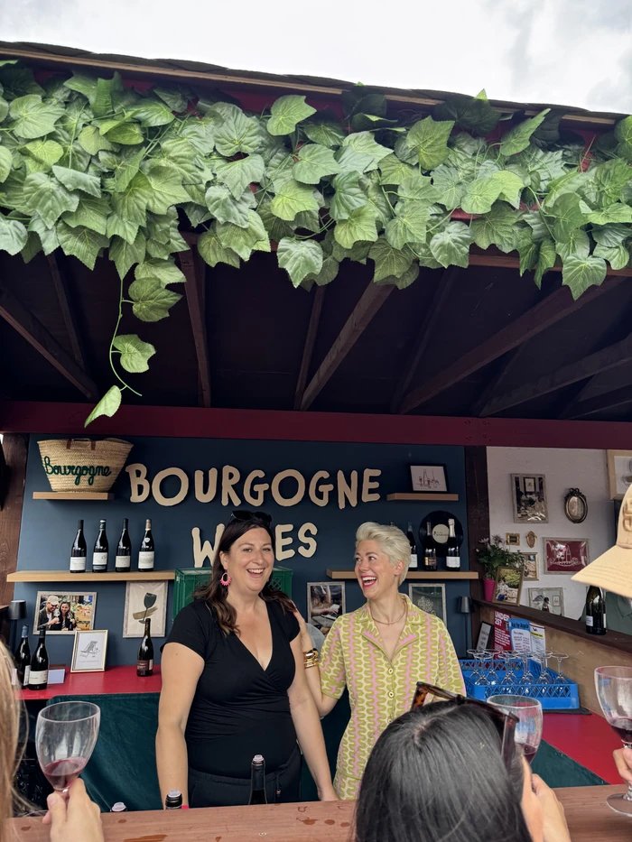 Two women presenting Bourgogne wines at a tasting stall, with guests holding wine glasses