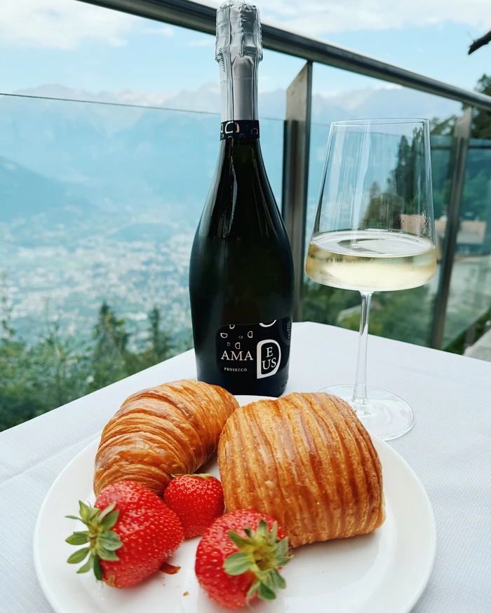 Prosecco bottle and glass with croissants and strawberries beside a scenic view