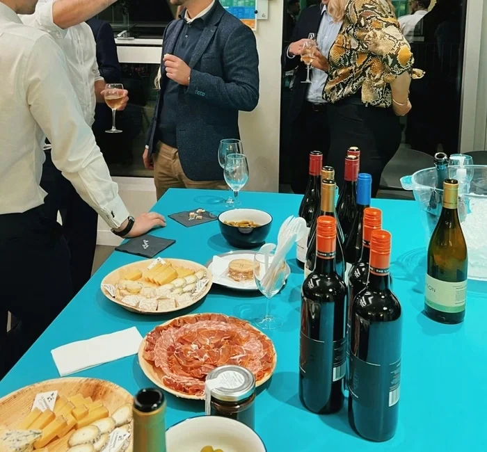 Guests mingle around a wine tasting table with bottles, glasses, cheese and charcuterie