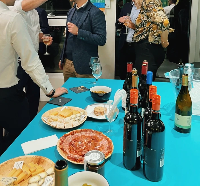Guests mingle around a wine tasting table with bottles, glasses, cheese and charcuterie