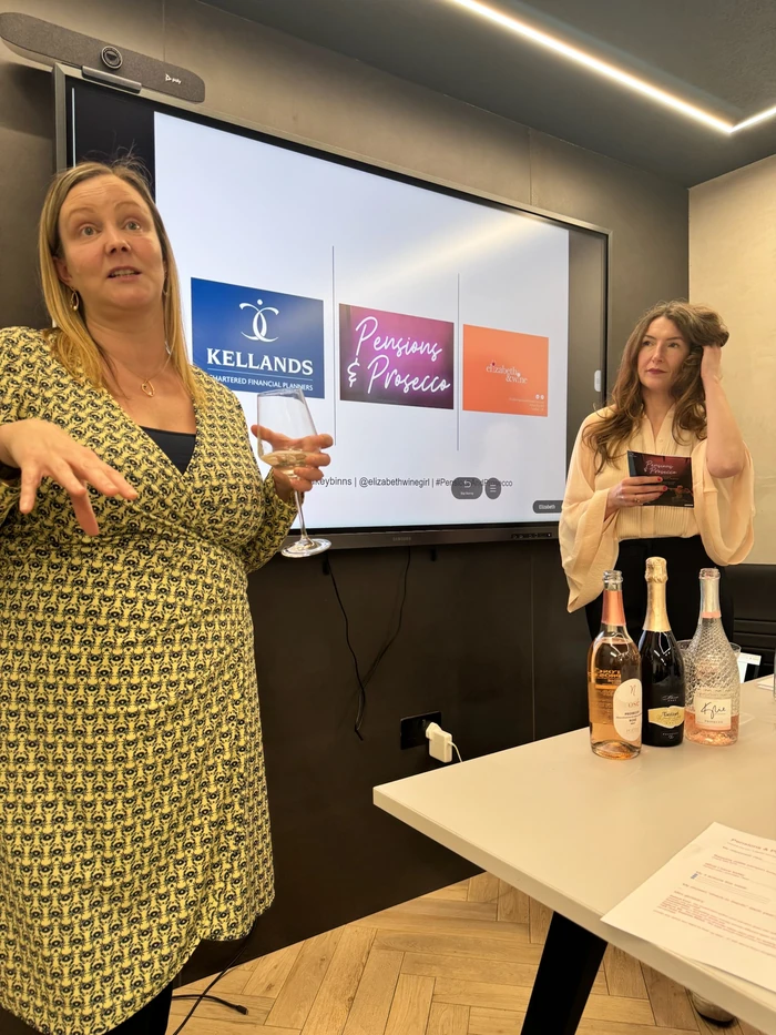 Wine presenter holding a glass beside a Pensions & Prosecco presentation screen
