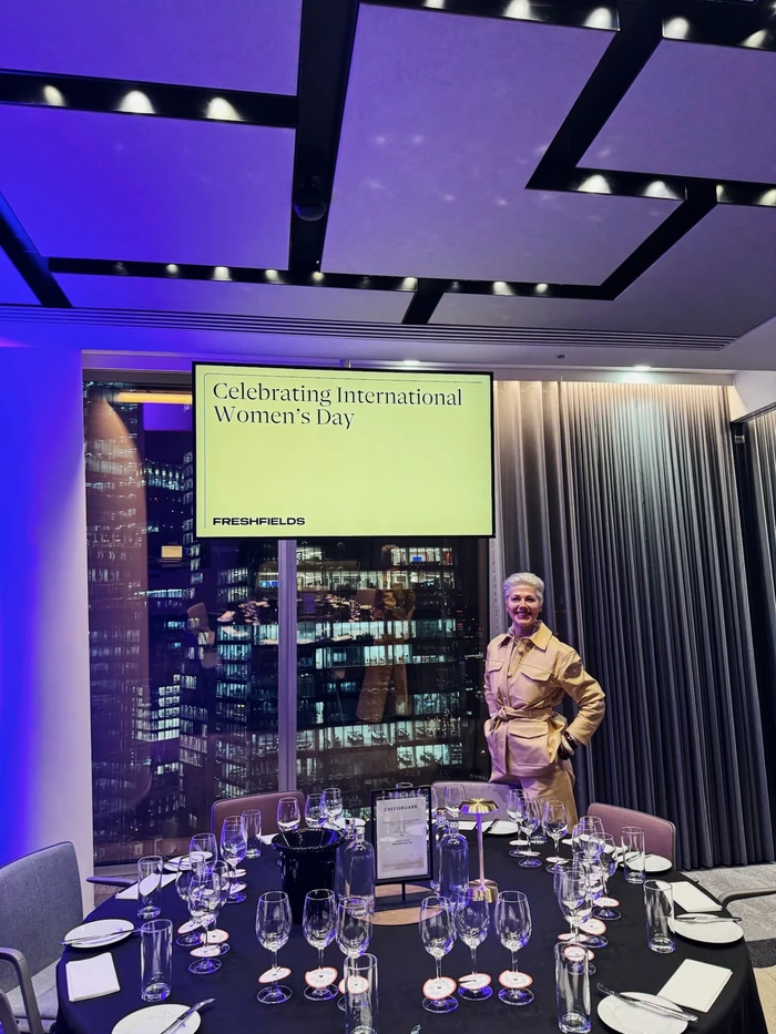Wine tasting table set for Freshfields' International Women's Day event, with a smiling host beside it