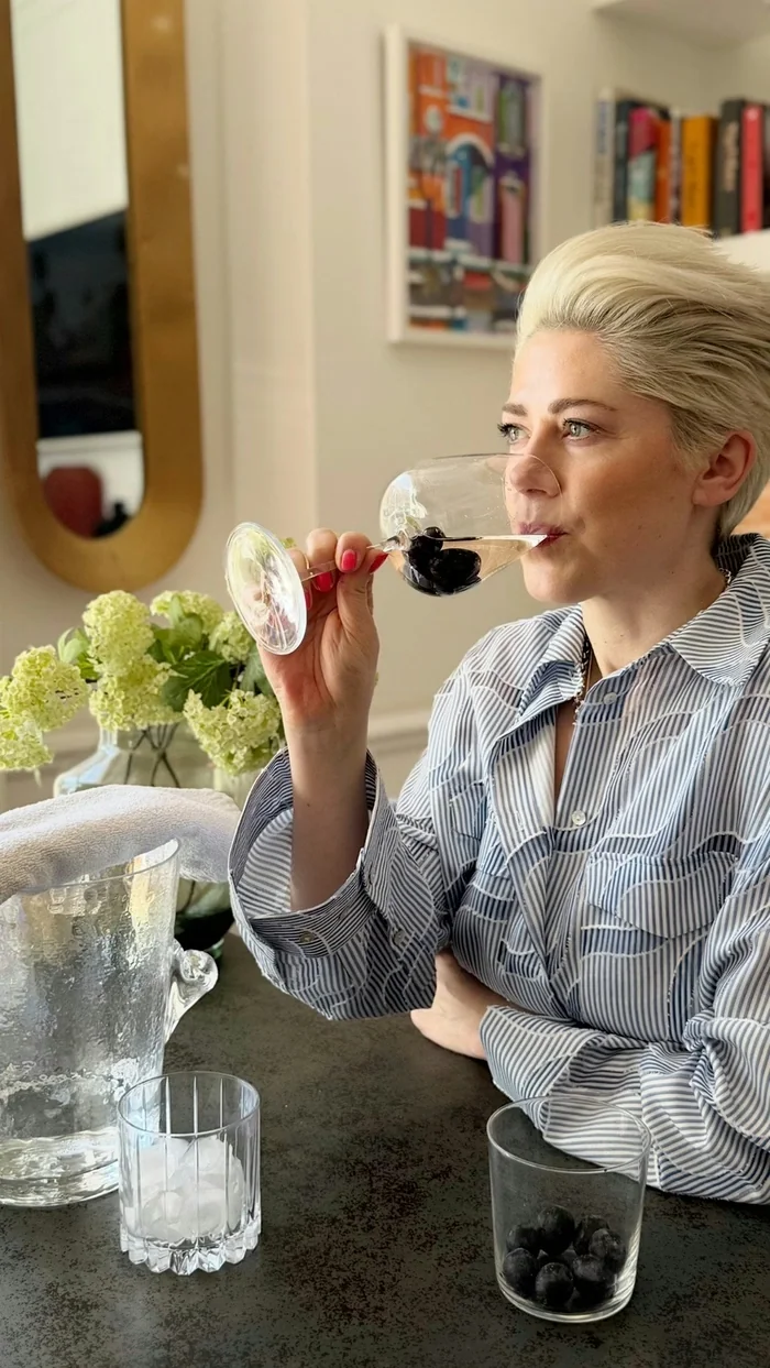 Woman tasting red wine beside an ice bucket and glass of blueberries