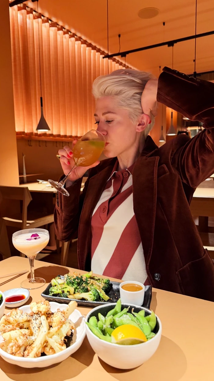 Person sipping a cocktail at a warmly lit restaurant table with sharing dishes
