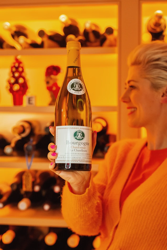 Bourgogne Chardonnay bottle held in front of a smiling person and illuminated shelves
