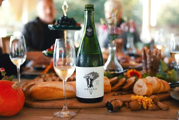 The Weyborne Estate Oriana sparkling wine bottle with filled glasses, bread and autumn produce on a dining table