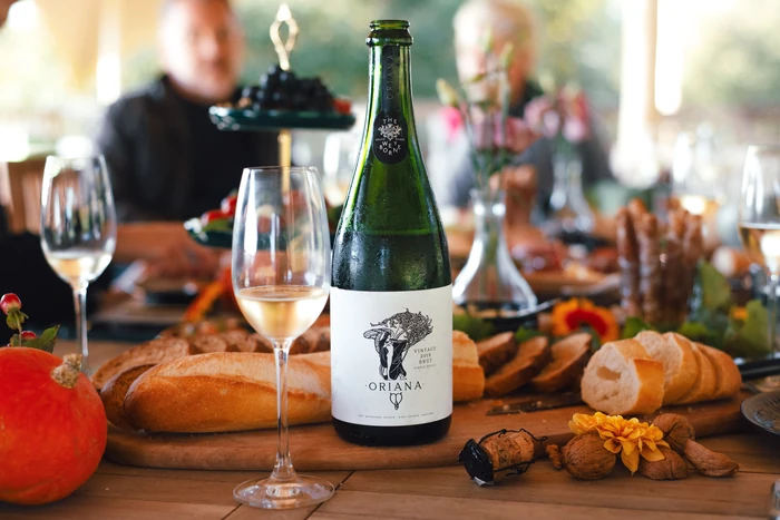 The Weyborne Estate Oriana sparkling wine bottle with filled glasses, bread and autumn produce on a dining table