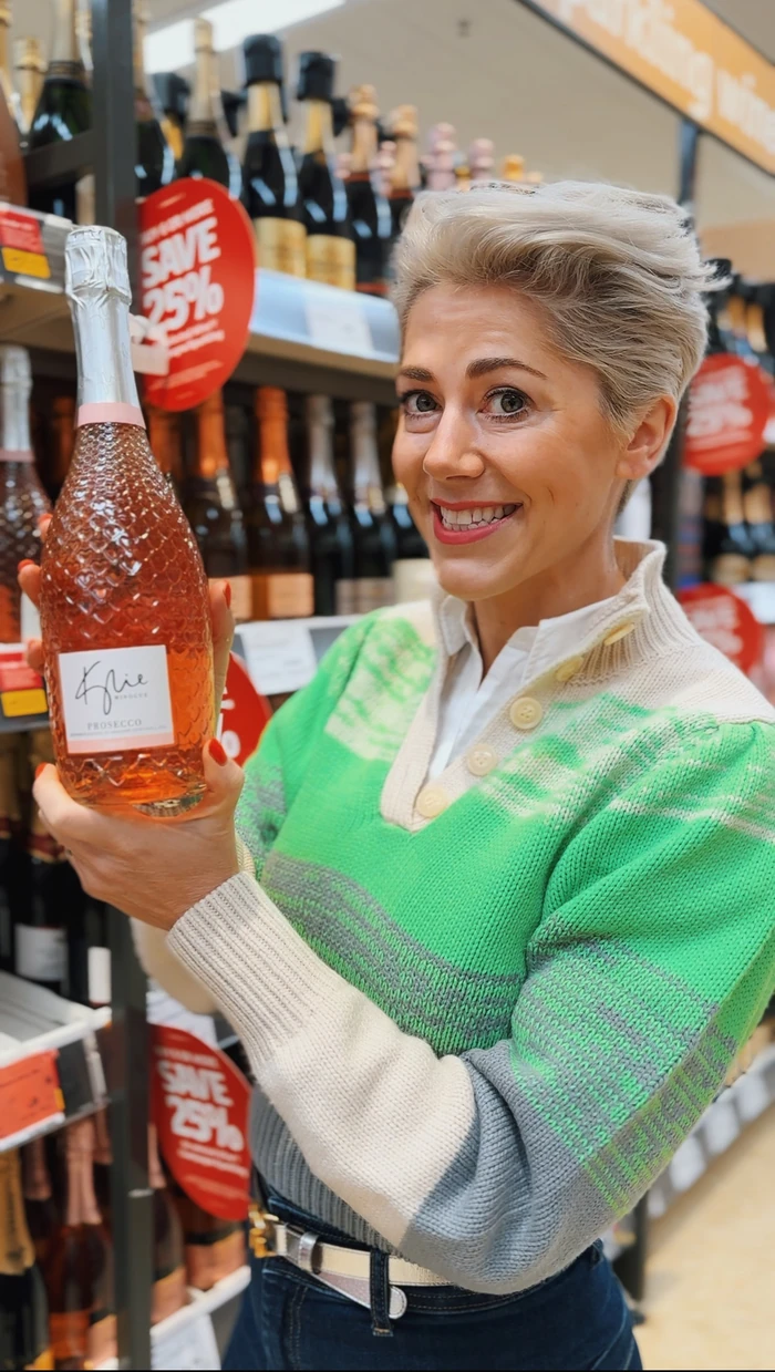 Smiling person holding a bottle of Kylie Prosecco in a wine shop
