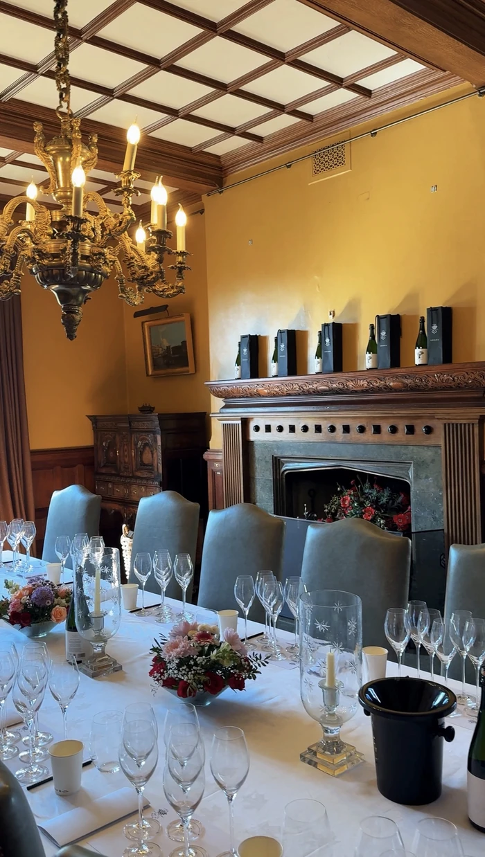 Elegant dining room set for a wine tasting, with wine glasses, flowers and bottles beside an ornate fireplace