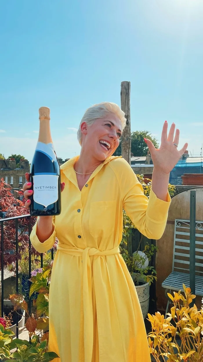 Smiling woman in a yellow dress holding a Nyetimber sparkling wine bottle outdoors