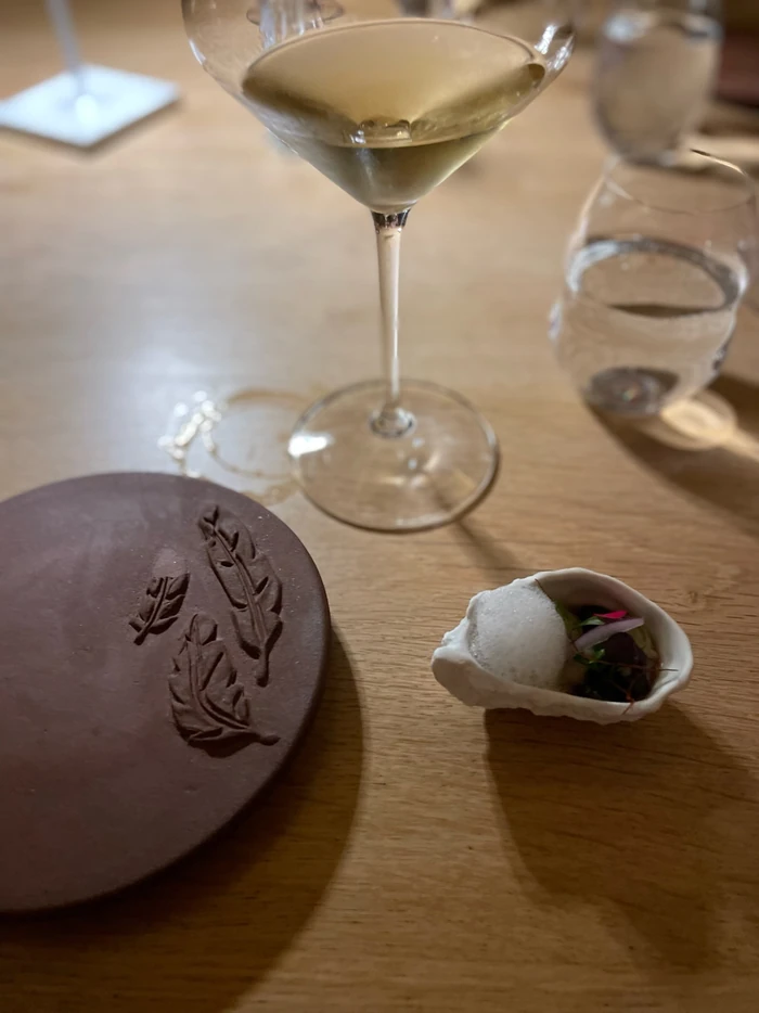 White wine in a stemmed glass beside tableware and a small plated dish
