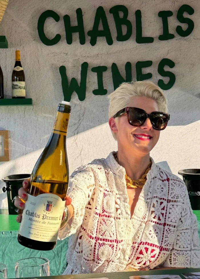Smiling woman holding a bottle of Chablis Premier Cru beneath a Chablis Wines sign
