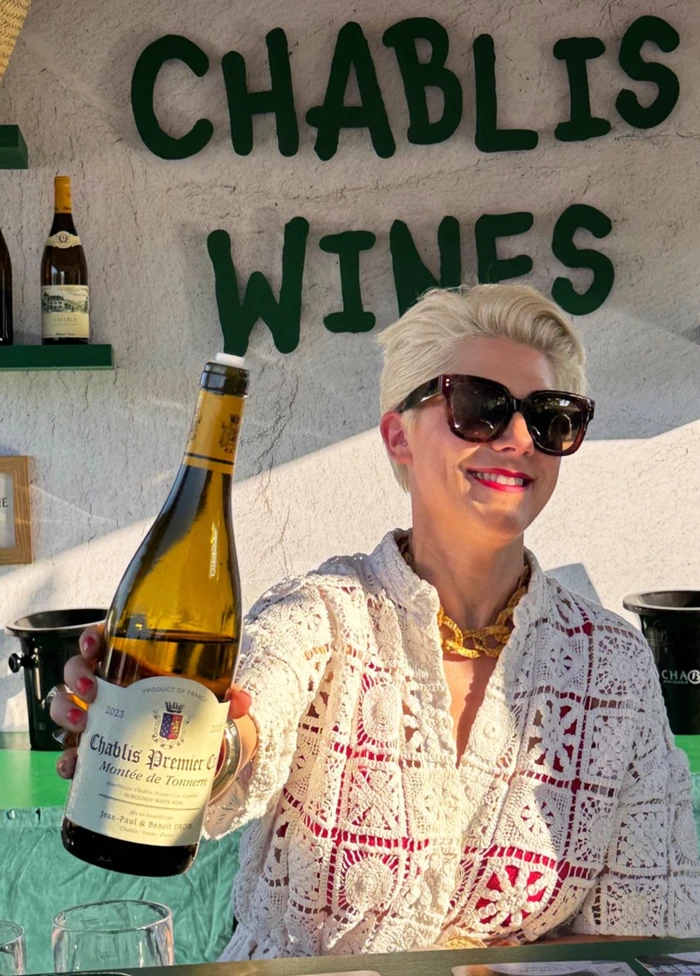 Smiling woman holding a bottle of Chablis Premier Cru beneath a Chablis Wines sign