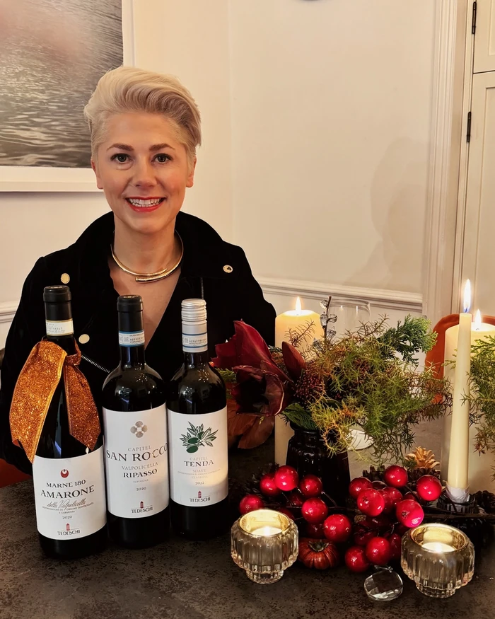 Smiling woman behind three Tedeschi wine bottles and a festive candlelit table setting