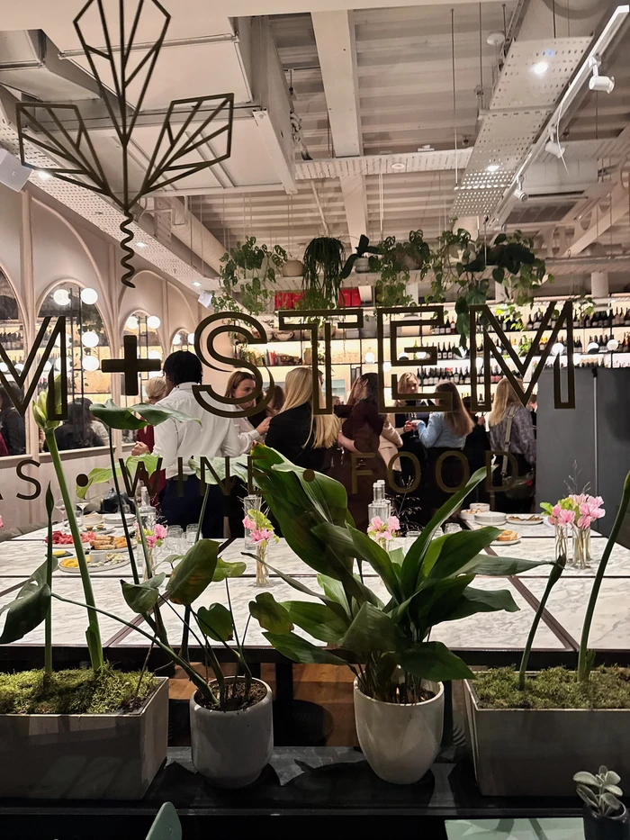 Dining room with plants, floral table settings and guests gathered around a restaurant bar