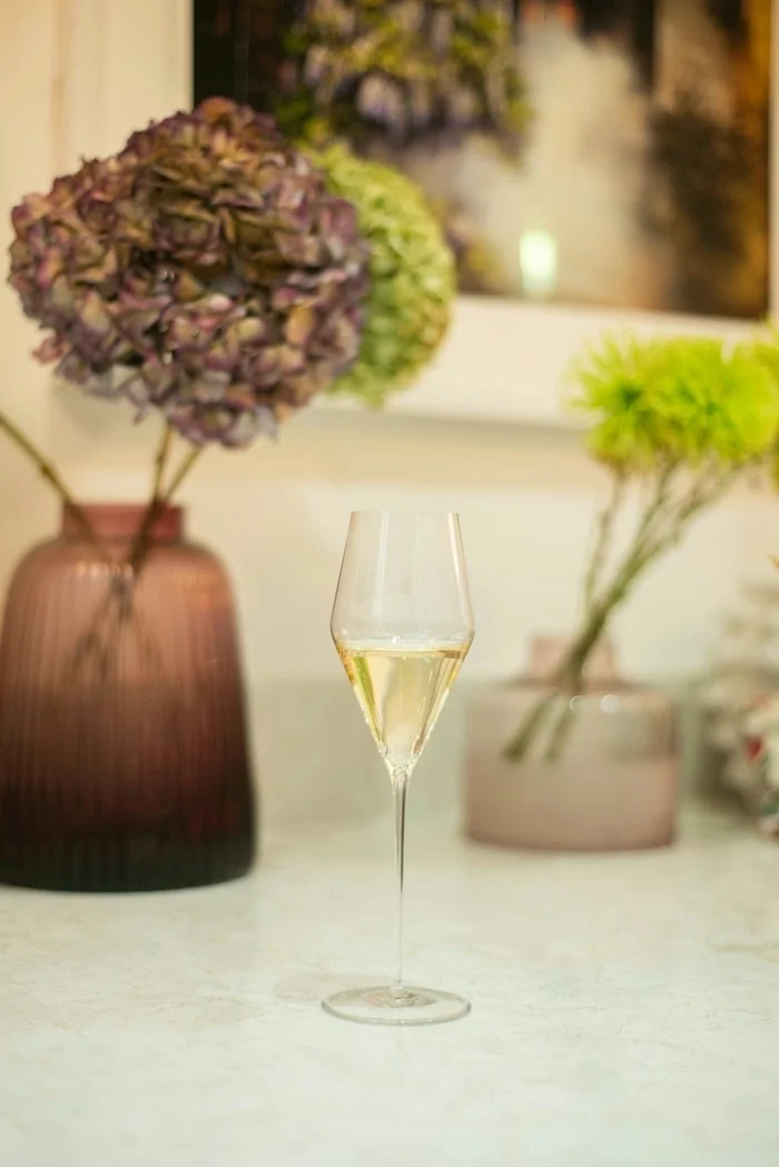Wine glass filled with pale wine beside pink and green flowers