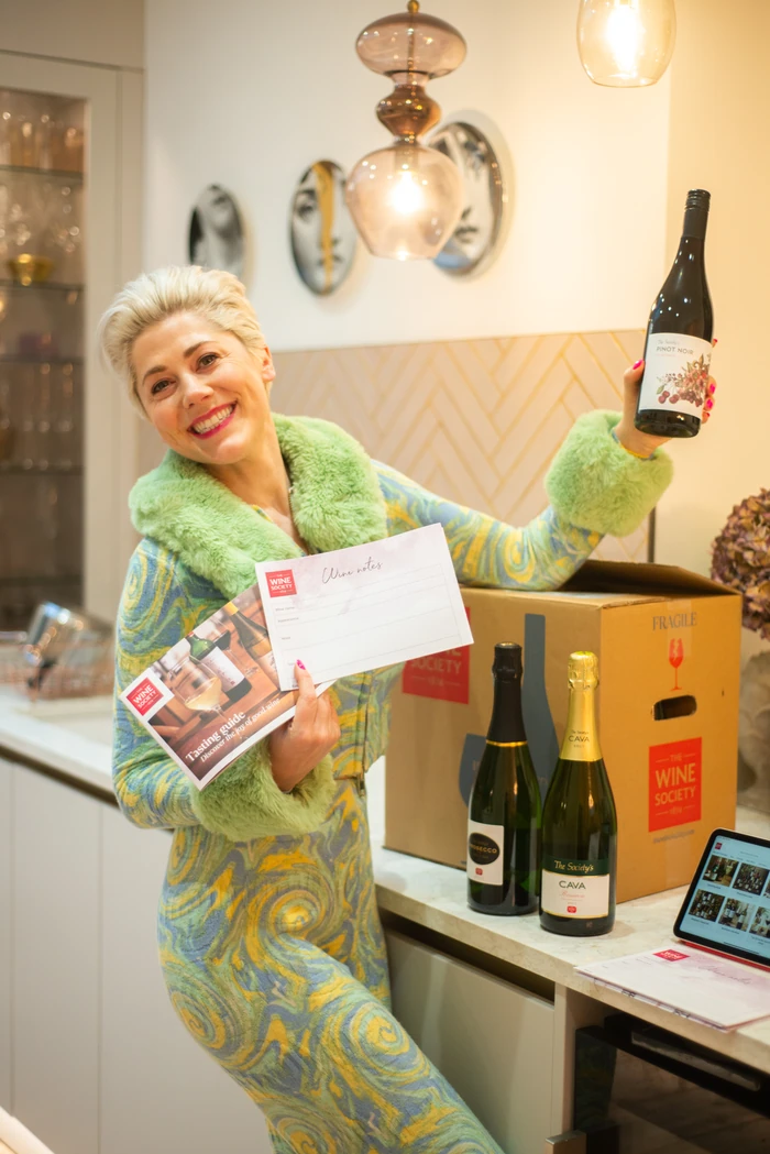 Smiling woman holding a bottle of Pinot Noir and Wine Society tasting materials beside wine boxes