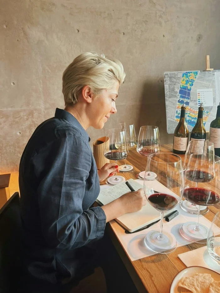 Woman tasting red wine and taking notes at a table with wine glasses and bottles