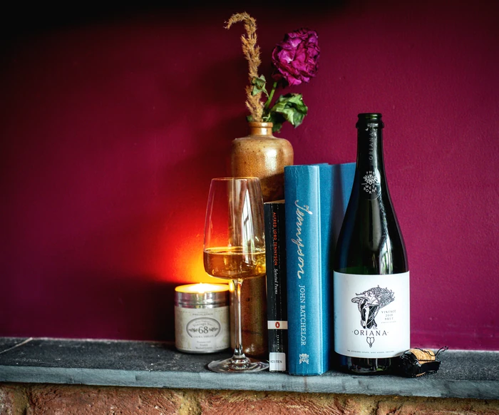 Bottle of English sparkling wine beside a filled glass, books, candle and dried flowers