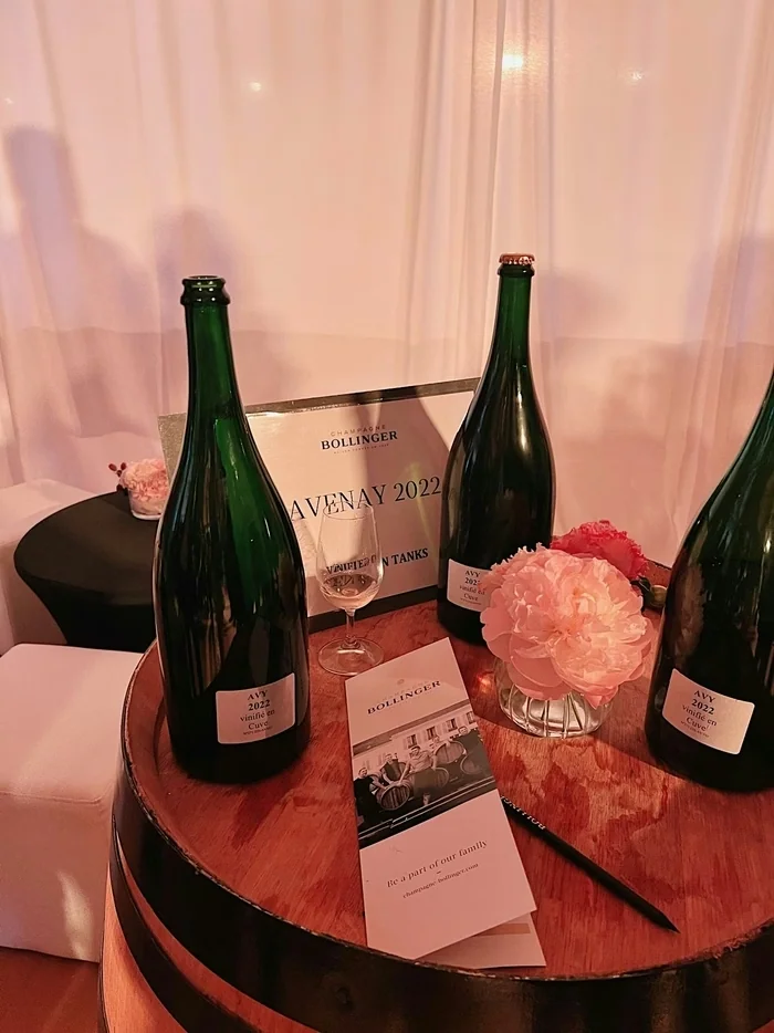 Bollinger champagne bottles and a tasting glass displayed with flowers on a wooden barrel