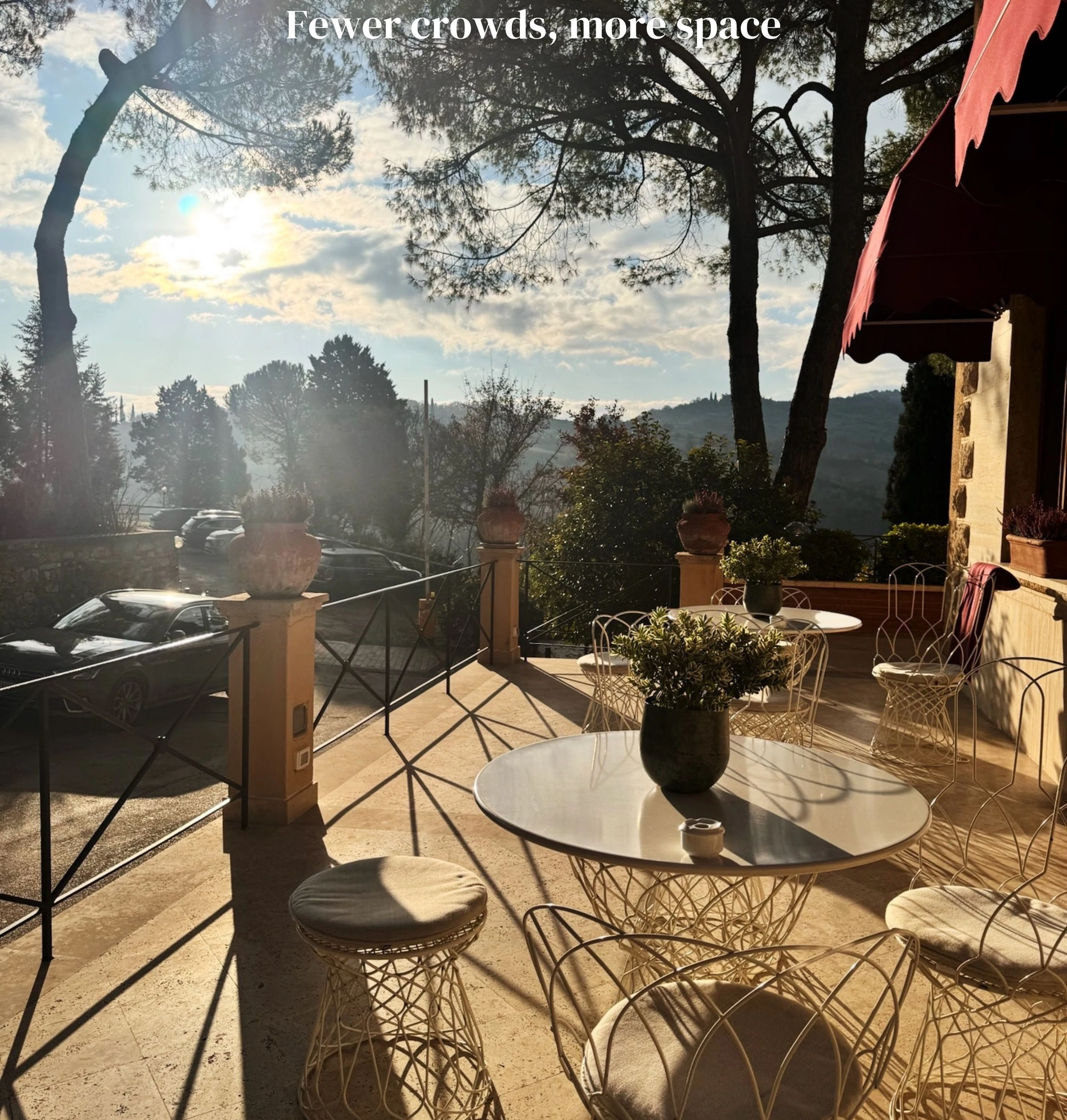 Sunlit hotel terrace with outdoor tables, pine trees and Tuscan hills beyond
