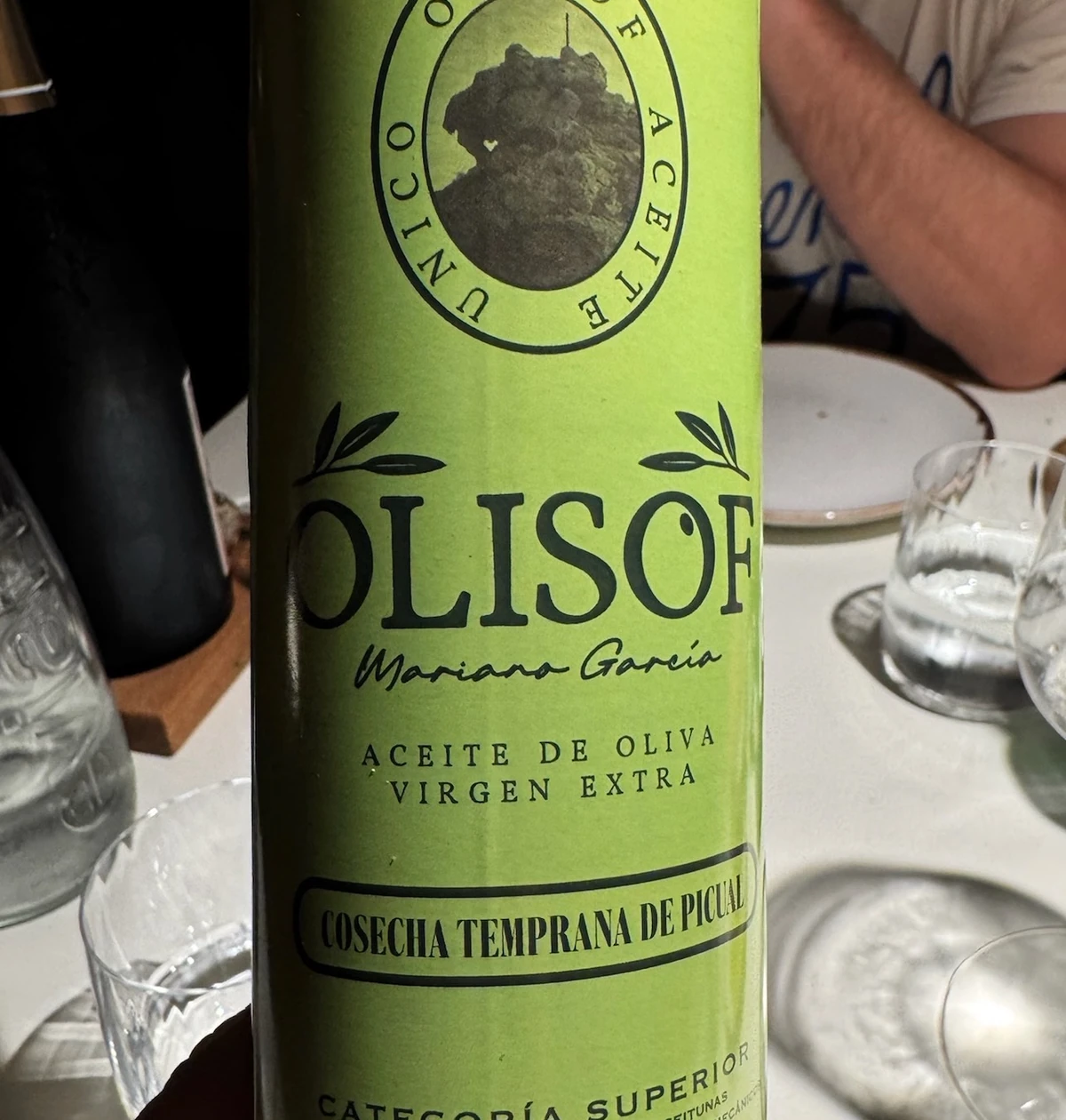 Bottle of Olisof extra virgin olive oil on a restaurant table, with glasses and diners in the background
