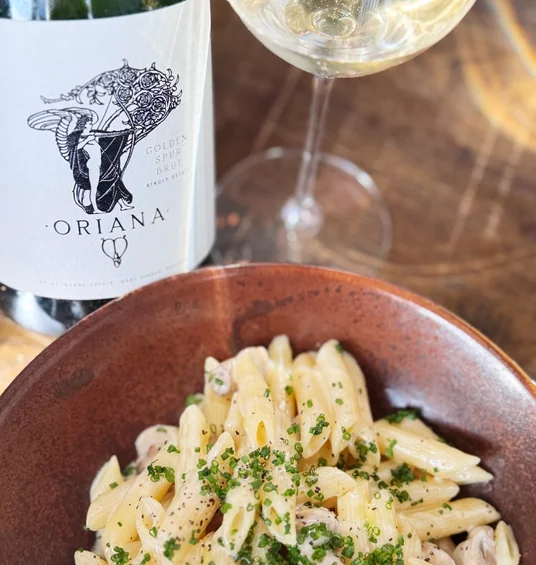 Oriana Golden Spur Brut beside a glass of sparkling wine and creamy pasta with herbs