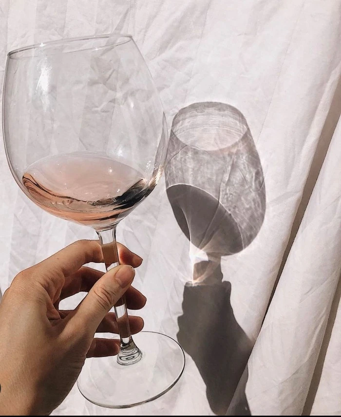 Hand holding a wine glass with rosé and shadow on fabric