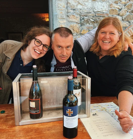 Three people pose behind two wine bottles and a tasting menu at a Tuscan winery
