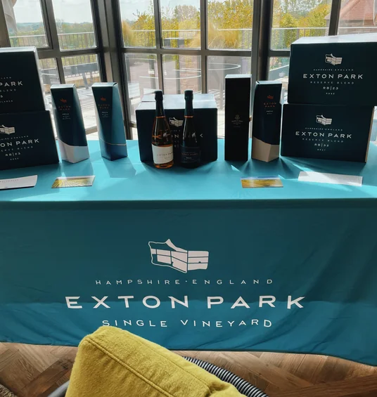 Exton Park wine bottles and boxes displayed on a branded table in a bright tasting room overlooking the vineyard