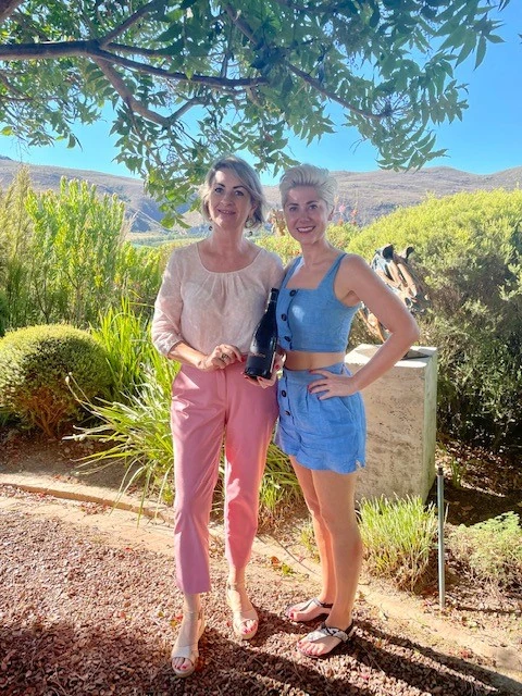 Two women holding a wine bottle in a sunny garden