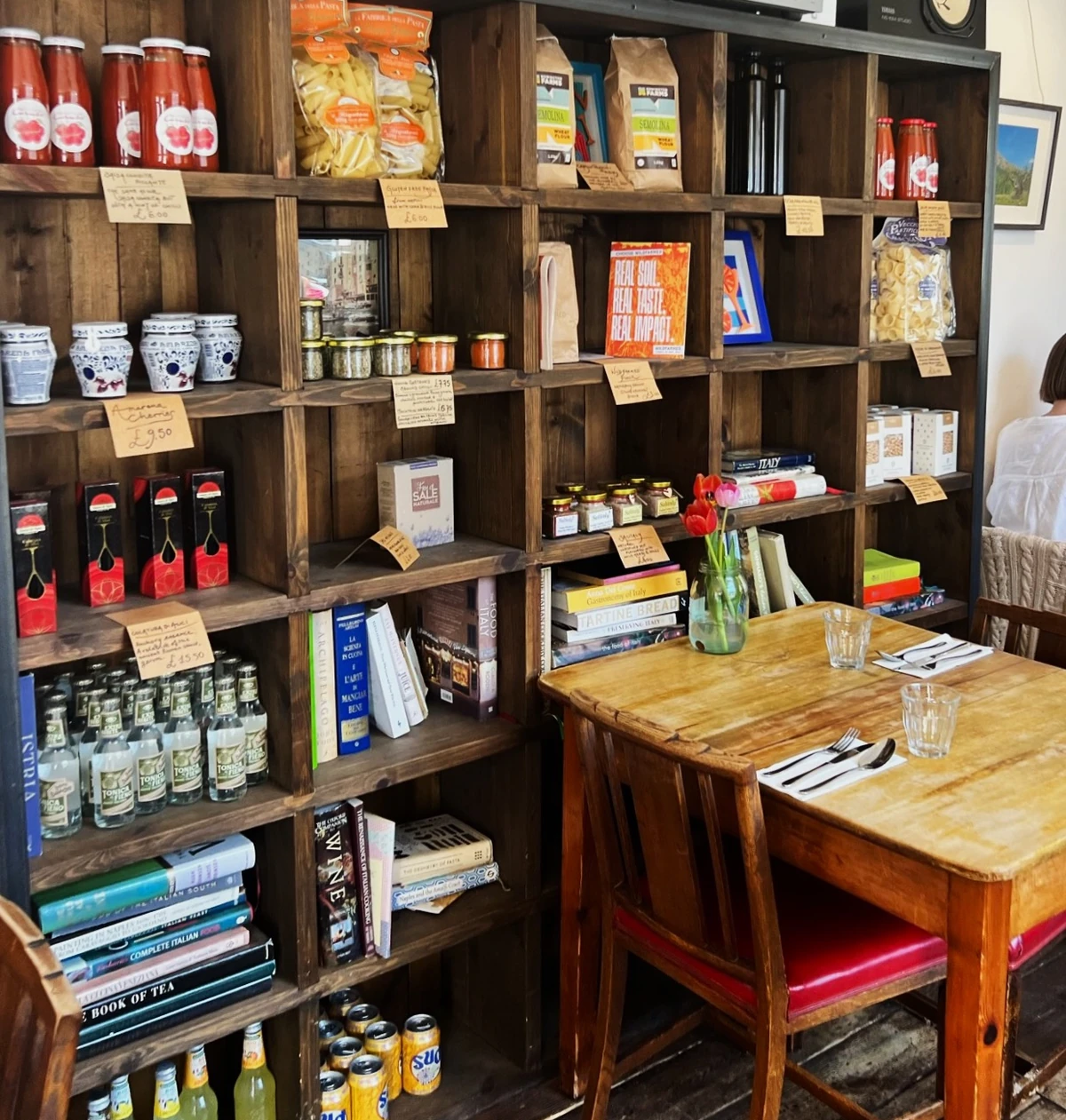 Italian deli shelves stocked with pasta, sauces, drinks and cookbooks beside a set dining table