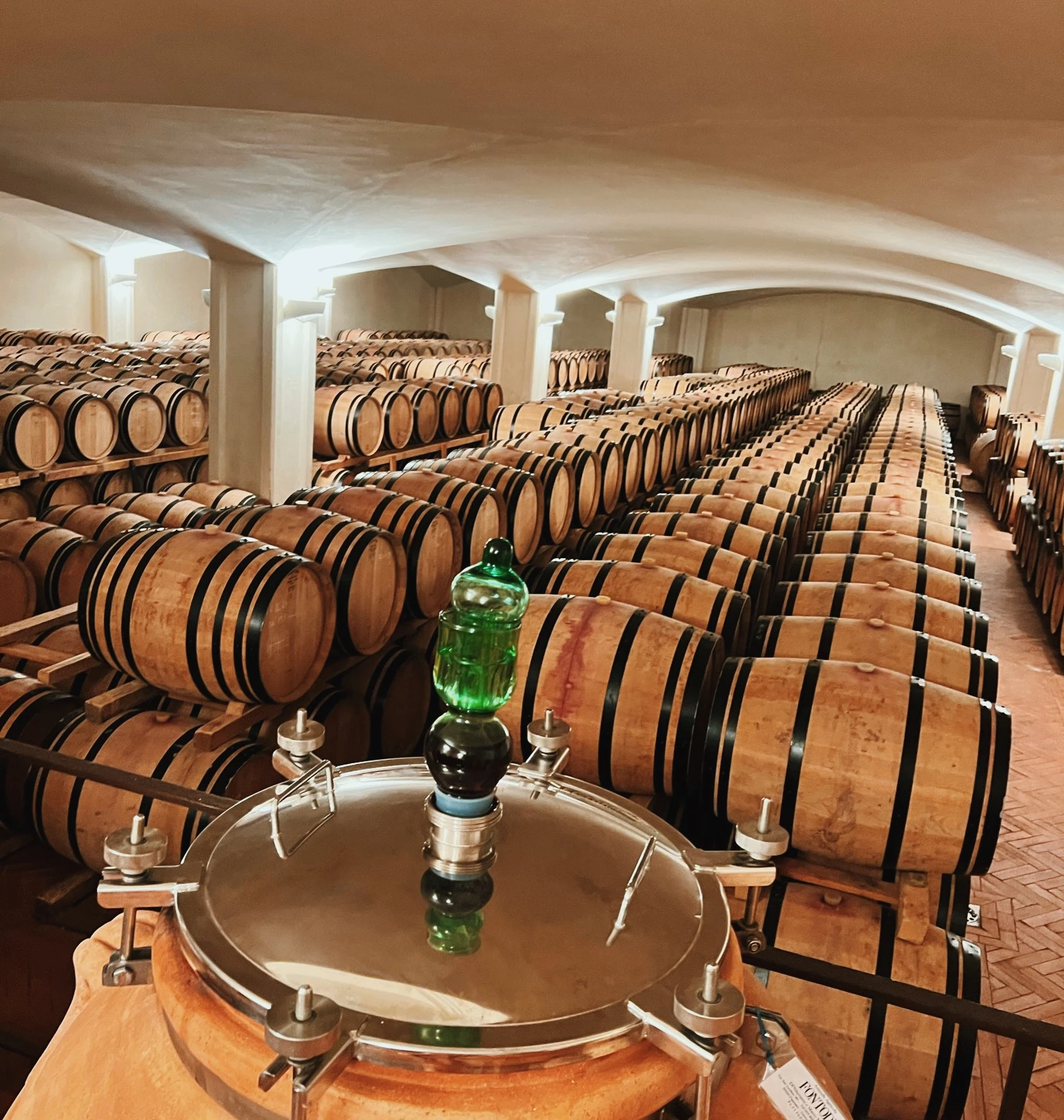 Rows of wine barrels in Fontodi Winery's cellar, with a stainless steel tank in the foreground