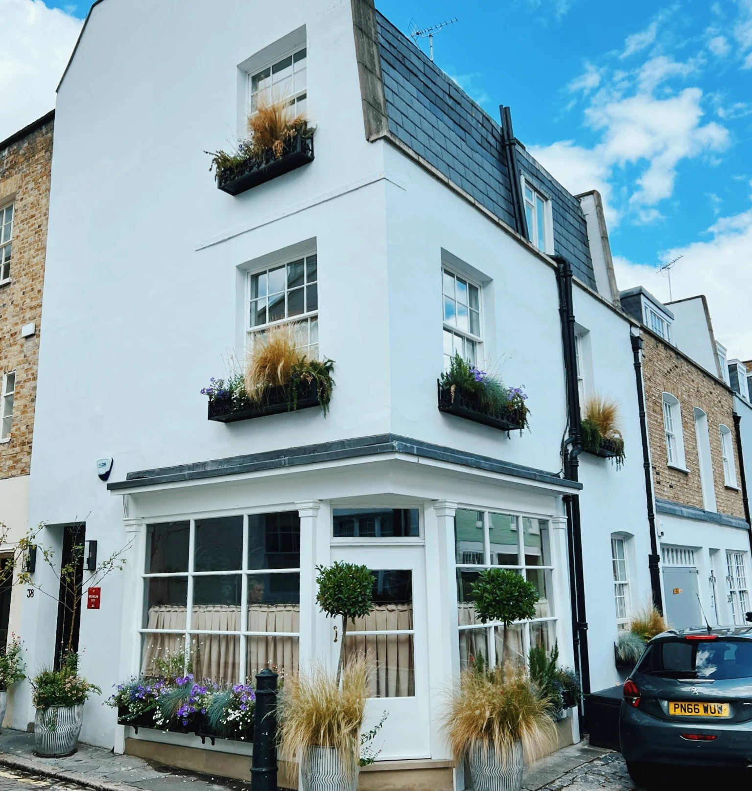White townhouse with flower boxes on a cobbled street beneath a bright blue sky