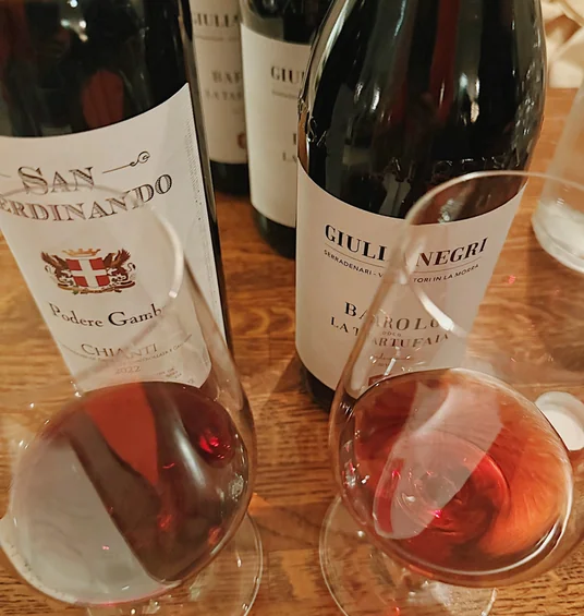Four bottles of red wine and two filled wine glasses on a wooden table at a tasting