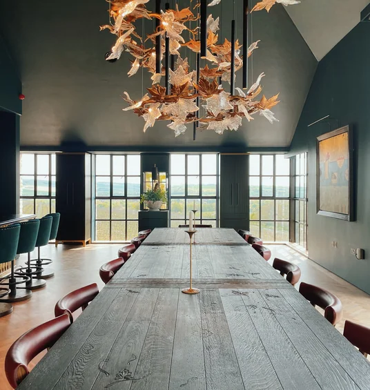 Dining room at Exton Park with a long wooden table, red chairs and a sculptural leaf chandelier