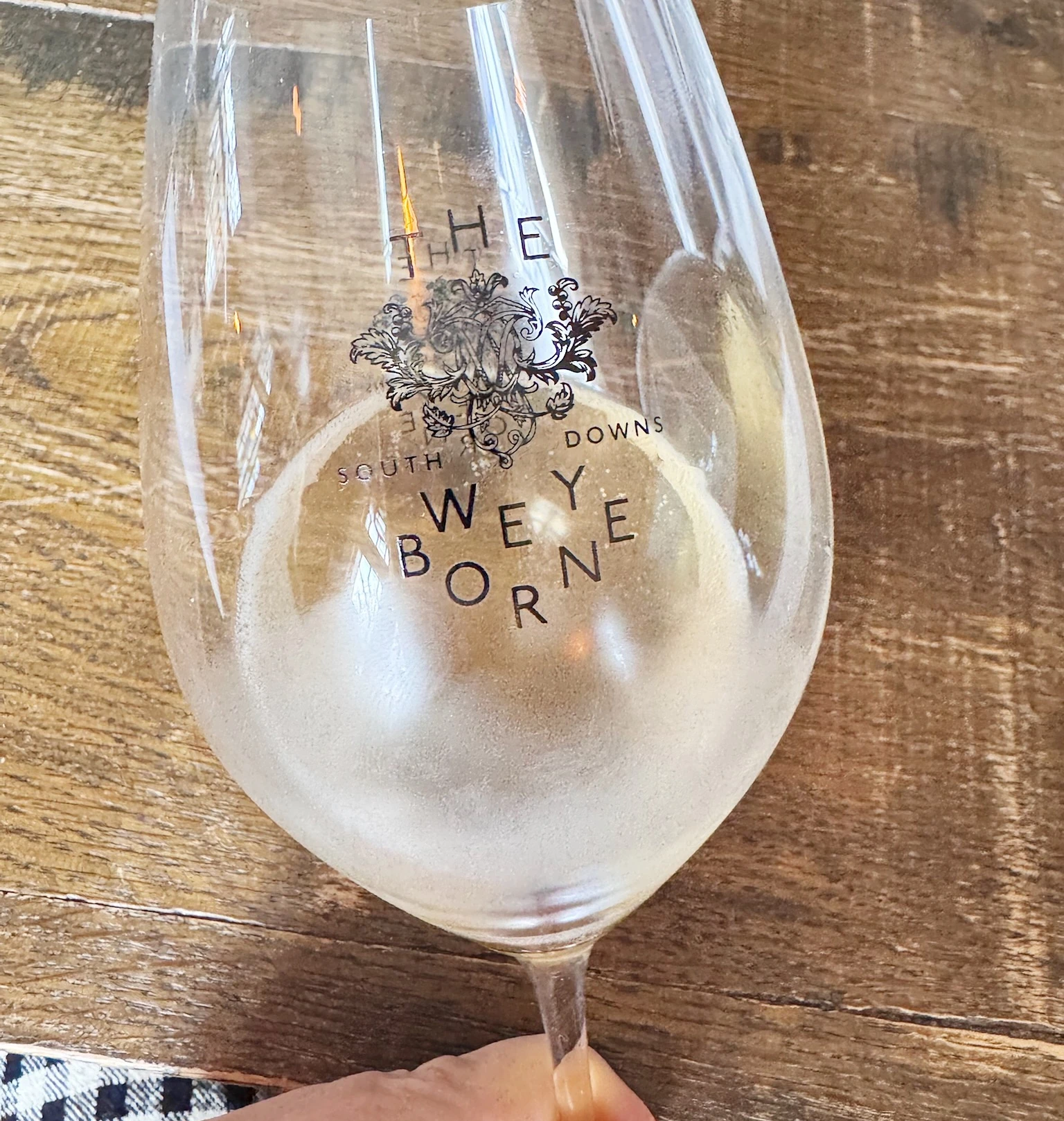 Wine glass with South Downs branding held over a wooden table