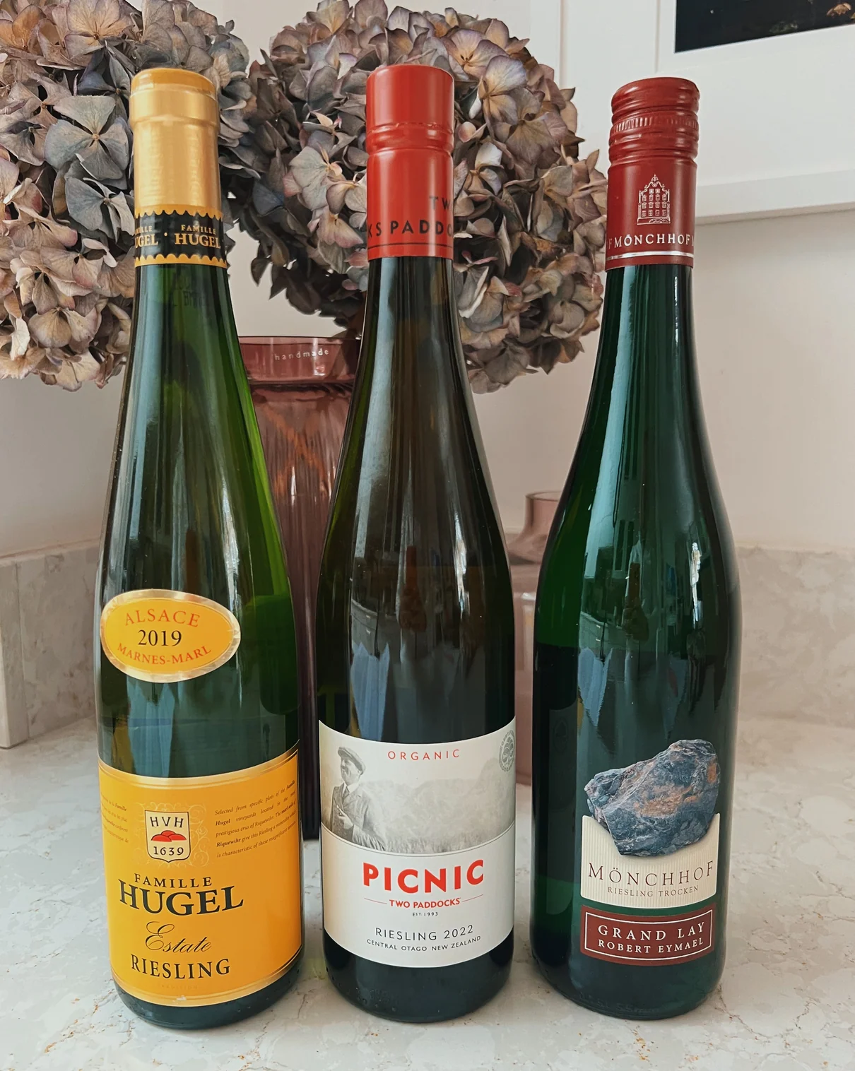 Three Riesling wine bottles with dried hydrangea wreath backdrop