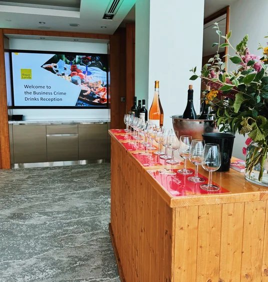 Wine tasting table with glasses, bottles and flowers beside a screen welcoming guests to a business drinks reception